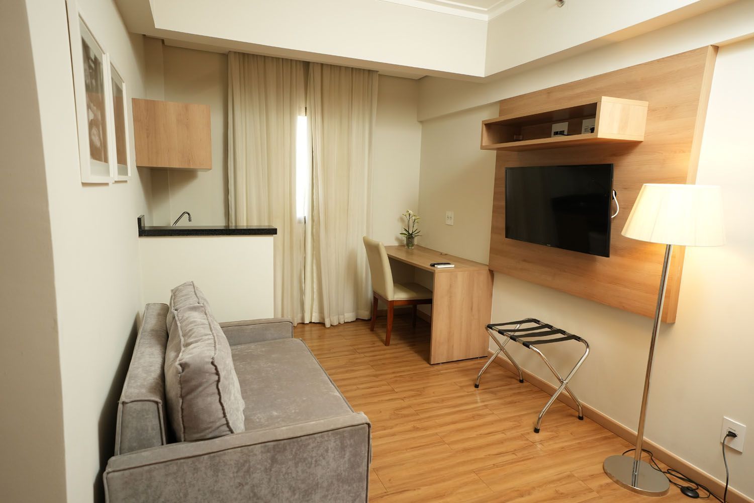 Uma sala de estar com sofá, escrivaninha, televisão e luminária.