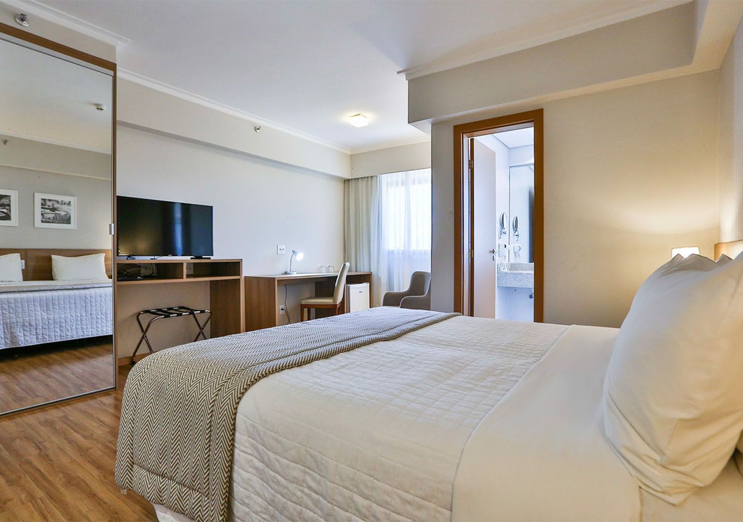 Um quarto de hotel com uma cama king size, escrivaninha, televisão e espelho.