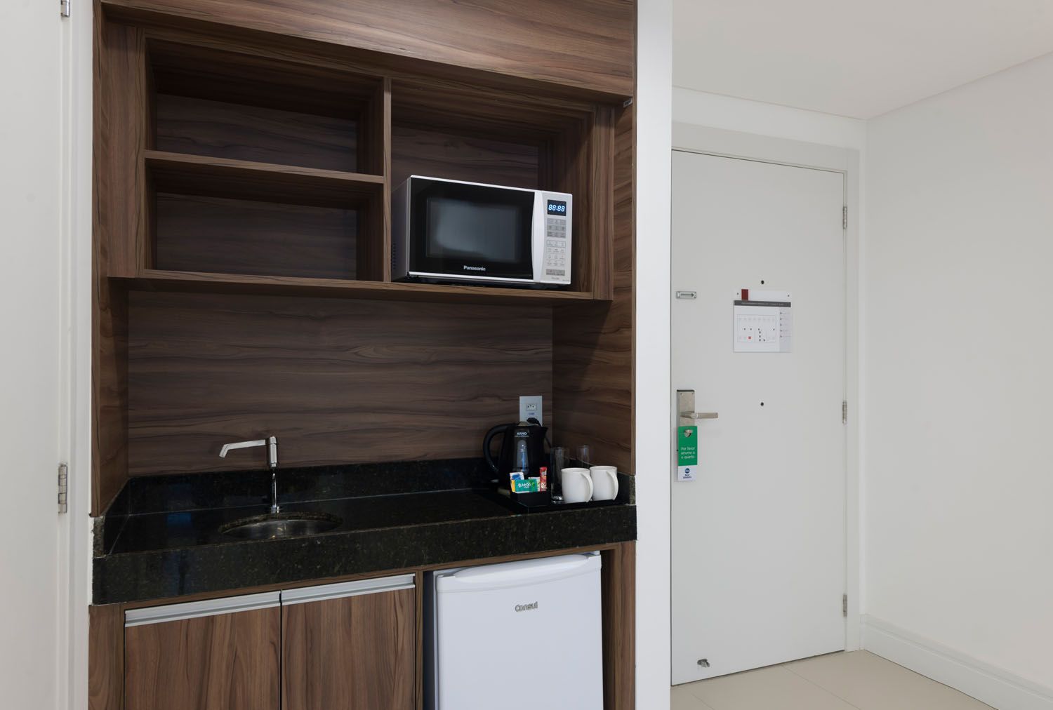 Um quarto de hotel com micro-ondas, pia e geladeira.