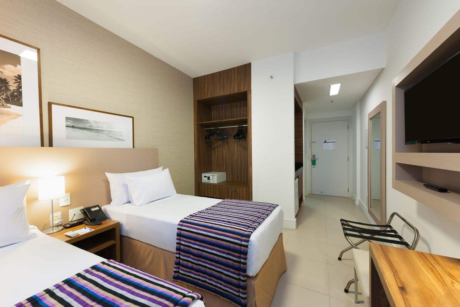 Um quarto de hotel com duas camas, uma escrivaninha e uma televisão.