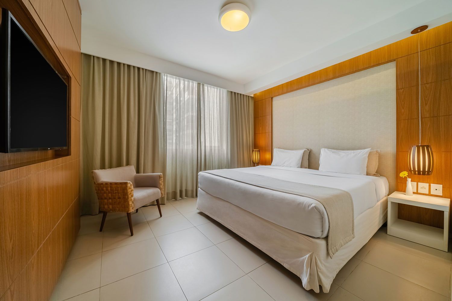 Um quarto de hotel com uma cama king size, cadeira e televisão.