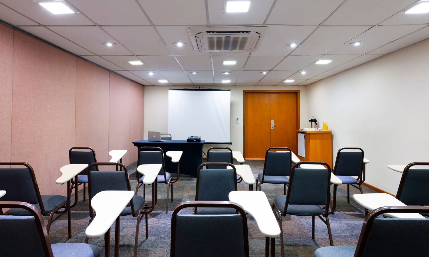 Uma sala de aula com mesas e cadeiras e uma tela de projetor