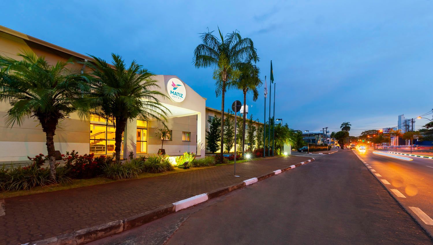 Um grande edifício com palmeiras na frente fica na beira de uma estrada.