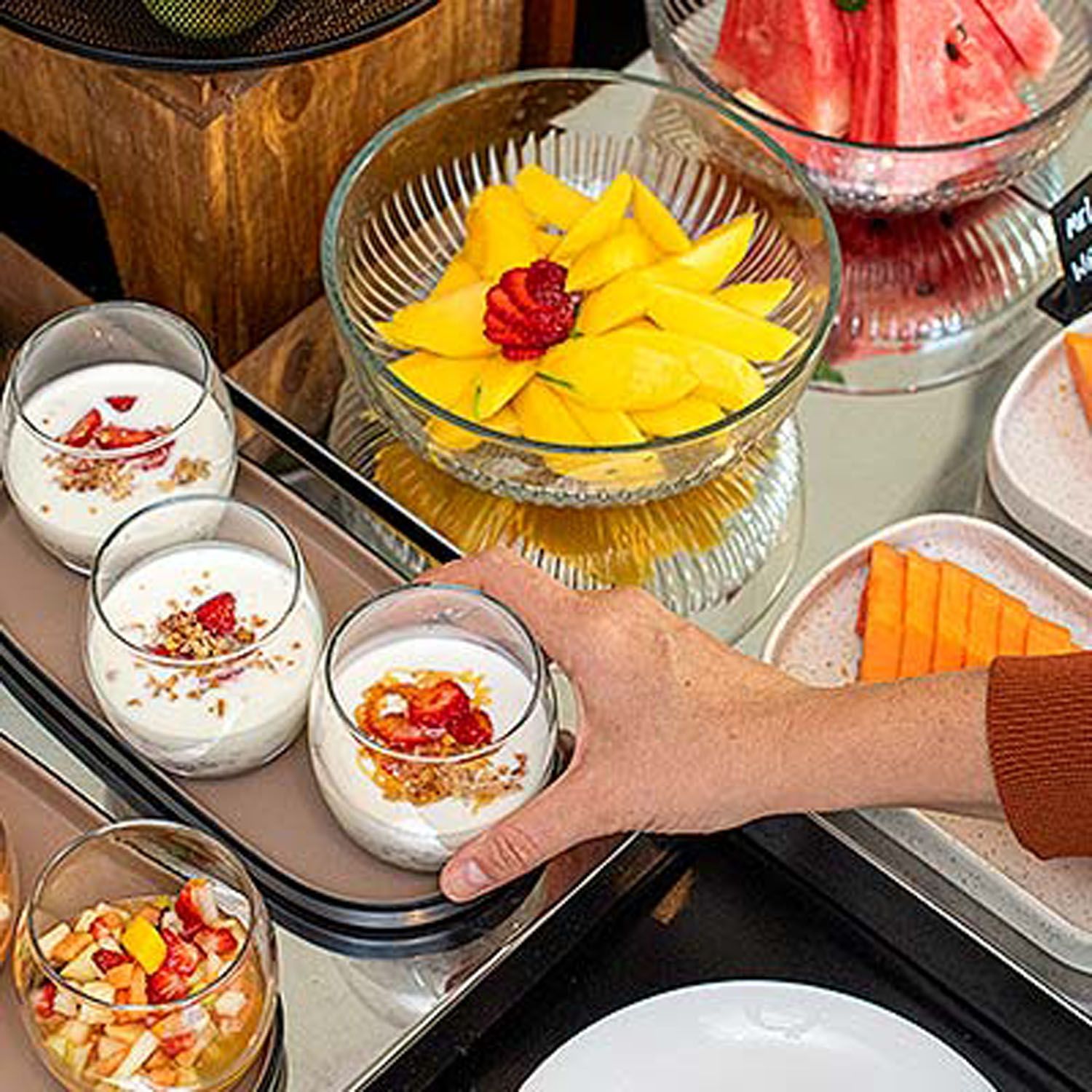 Uma pessoa está segurando um copo de iogurte ao lado de uma tigela de frutas.