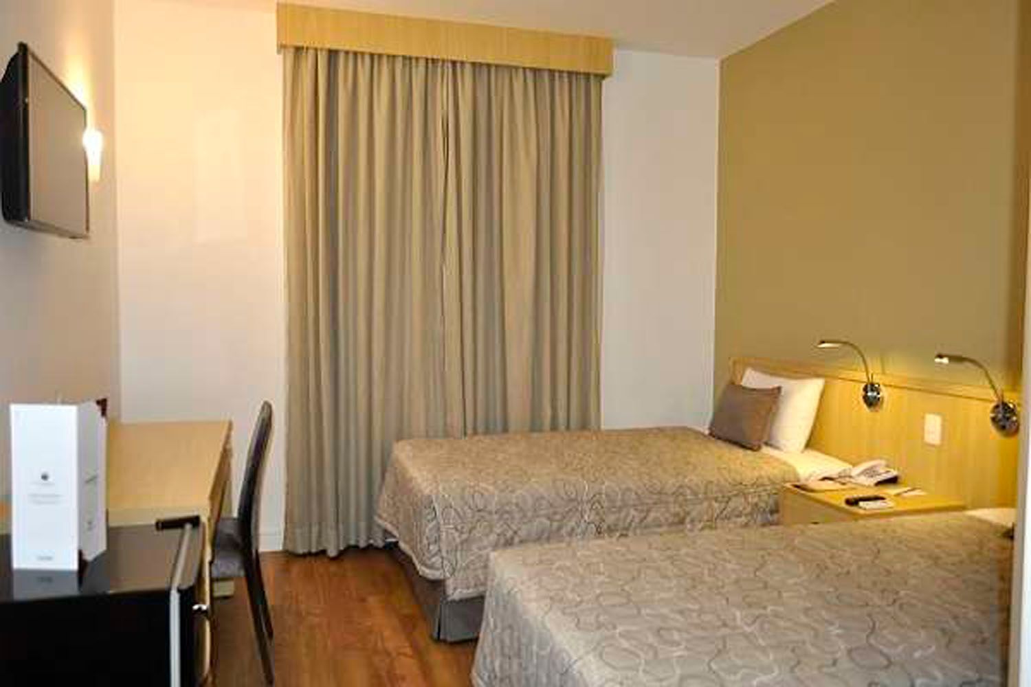 Um quarto de hotel com duas camas, uma escrivaninha e uma TV de tela plana.