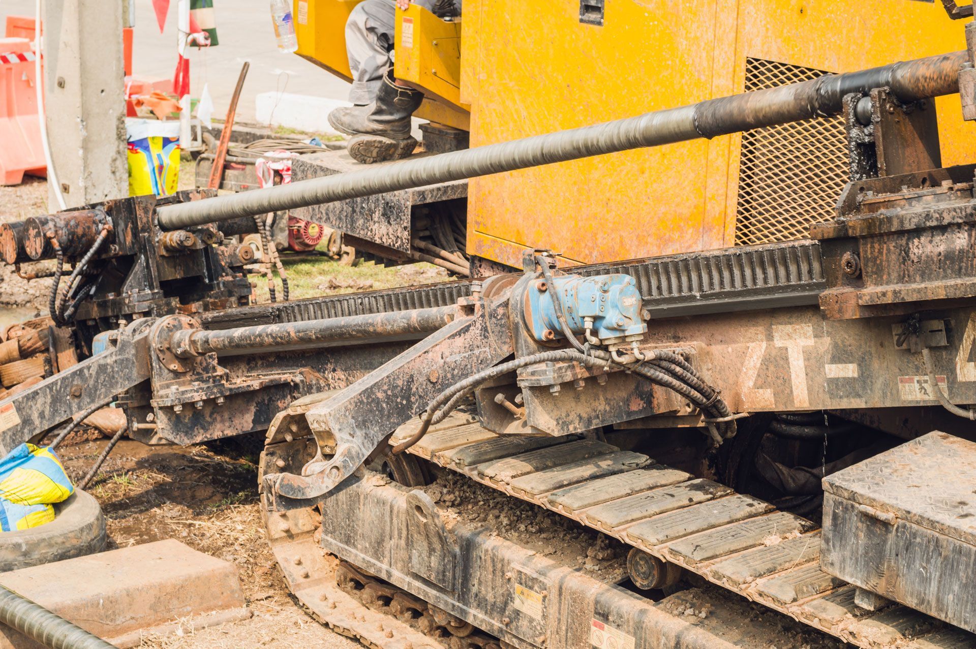 Yellow construction machine drilling on a work site, muddy ground.