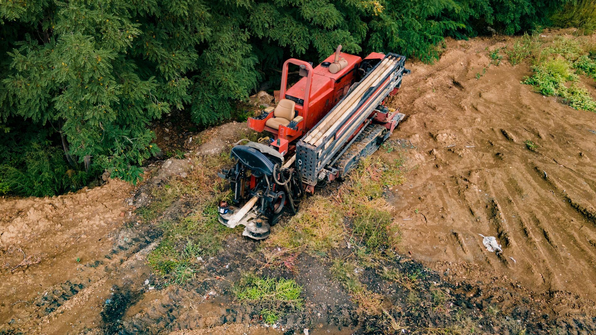 Red drilling machine on muddy ground near green trees
