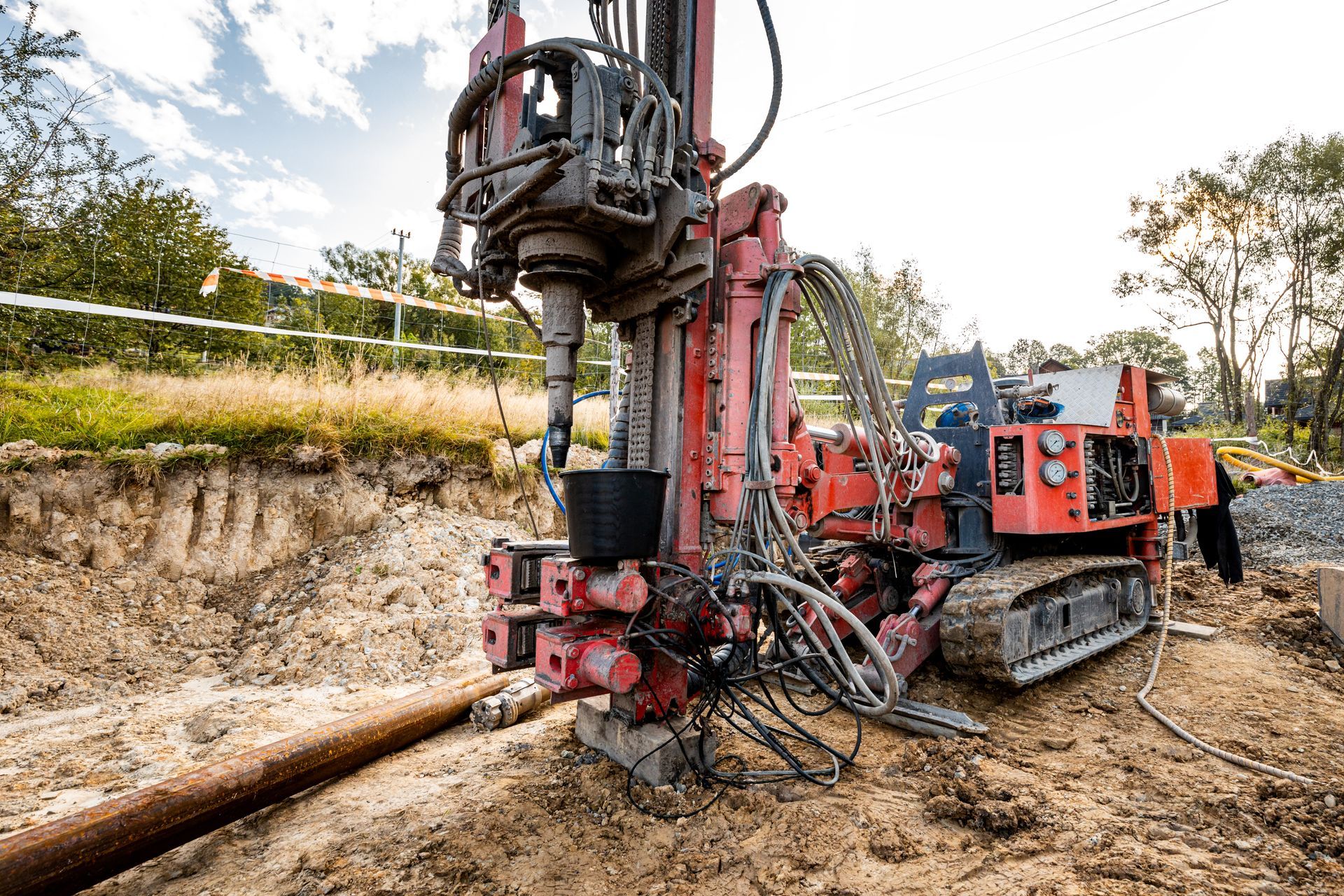 Red drilling machine on a construction site boring into the ground near a pipe