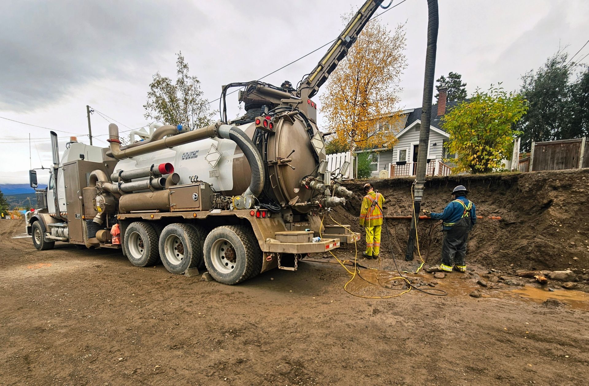 A large truck with a tank and two workers near a power pole on a muddy hillside