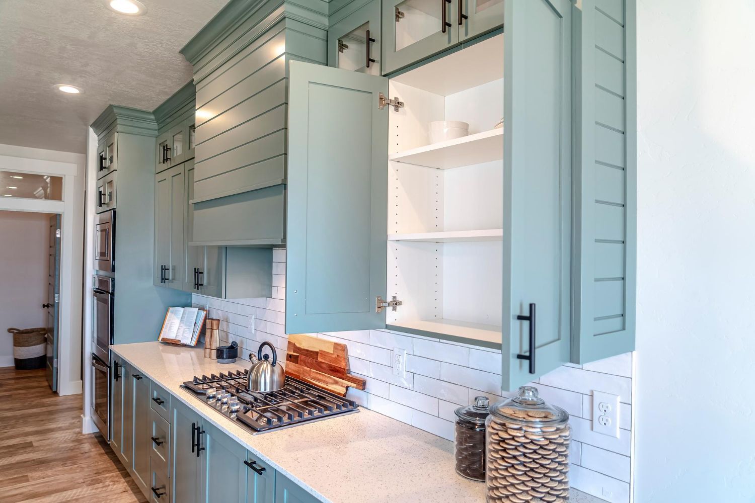 Blue kitchen cabinets with one door open, countertop, and cooktop.