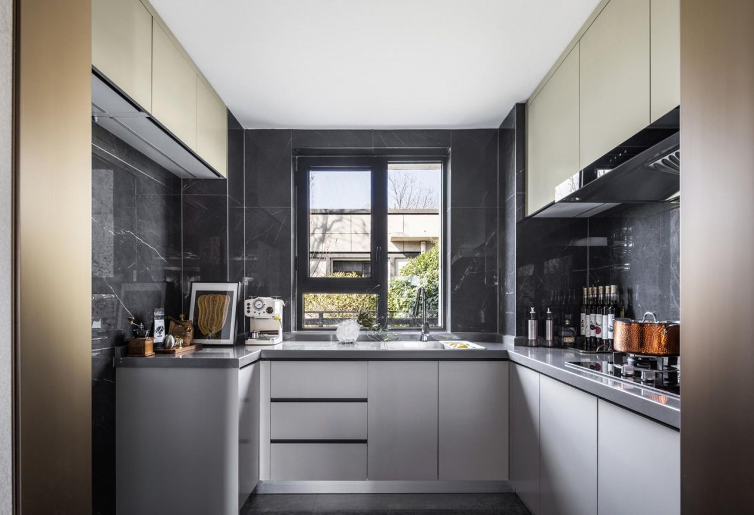 Modern gray kitchen with window, dark marble backsplash, light cabinets, and stainless steel appliances.