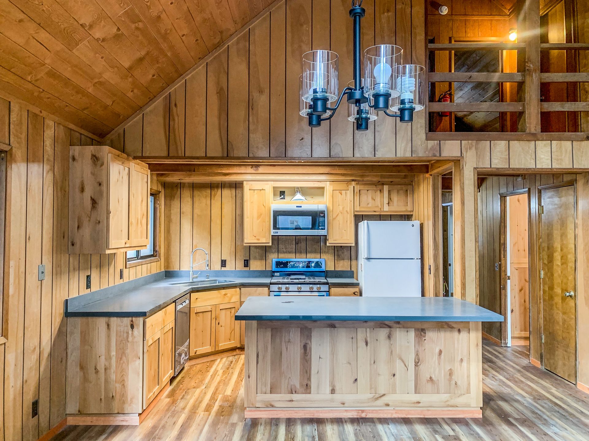 Wooden kitchen with cabinets, countertops, and an island. Appliances include a stove, microwave, and refrigerator.