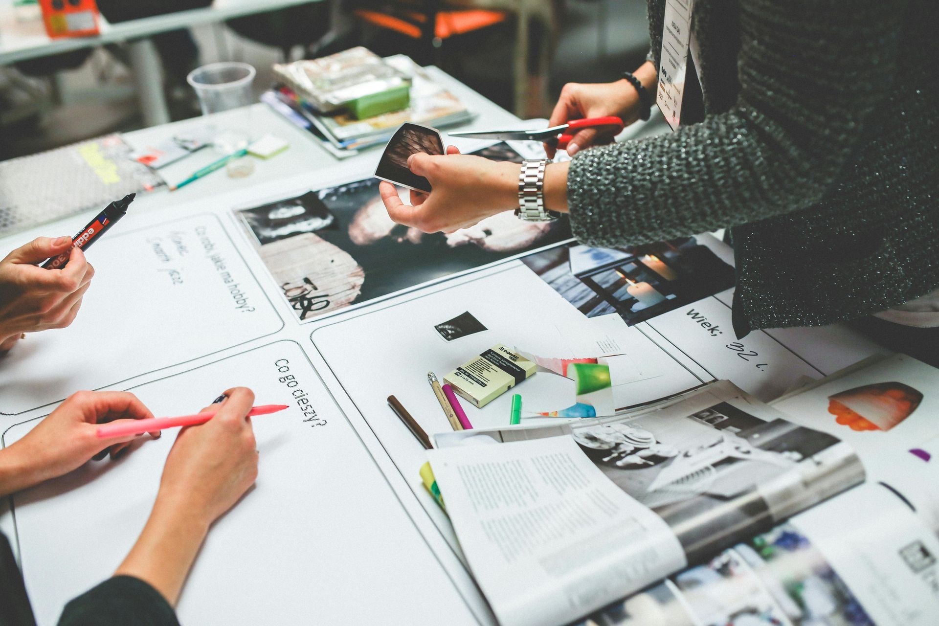Hands cutting, writing, and arranging photos on a large paper, collaborative creative project.