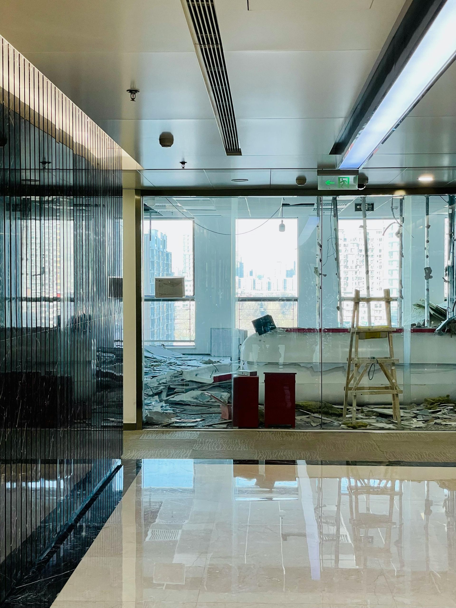 Interior of a building in disrepair; shattered glass and debris on the floor, red fire extinguisher.
