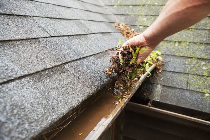 Une personne nettoie une gouttière sur le toit d'une maison.