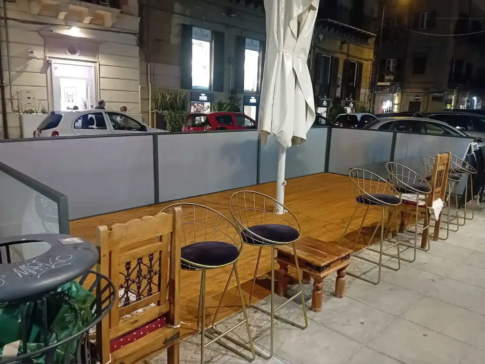 Area salotto all'aperto con sedie e ombrellone parzialmente aperto; di notte.