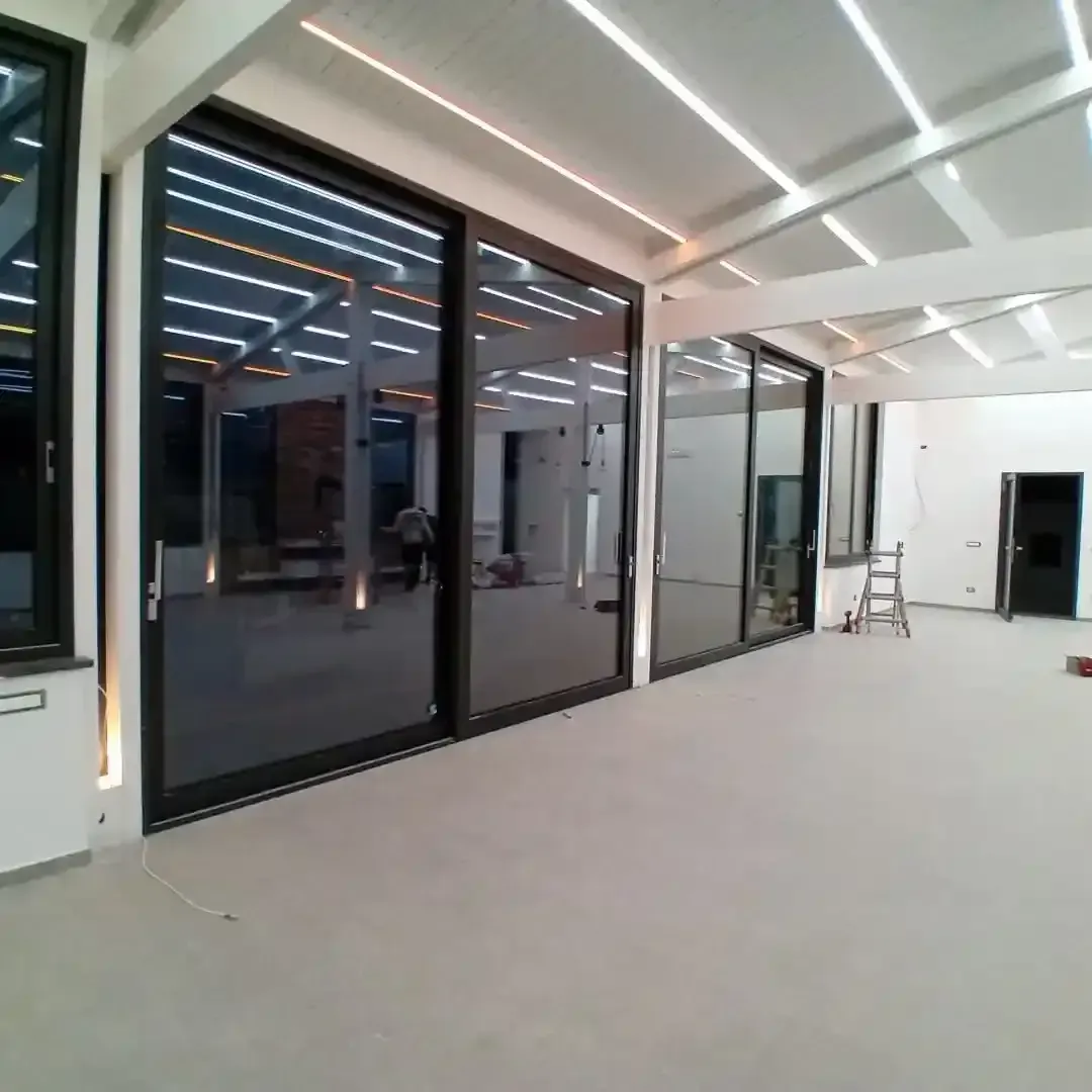 Porte e finestre in vetro in una stanza luminosa con luci da incasso nel soffitto e pavimento grigio chiaro.