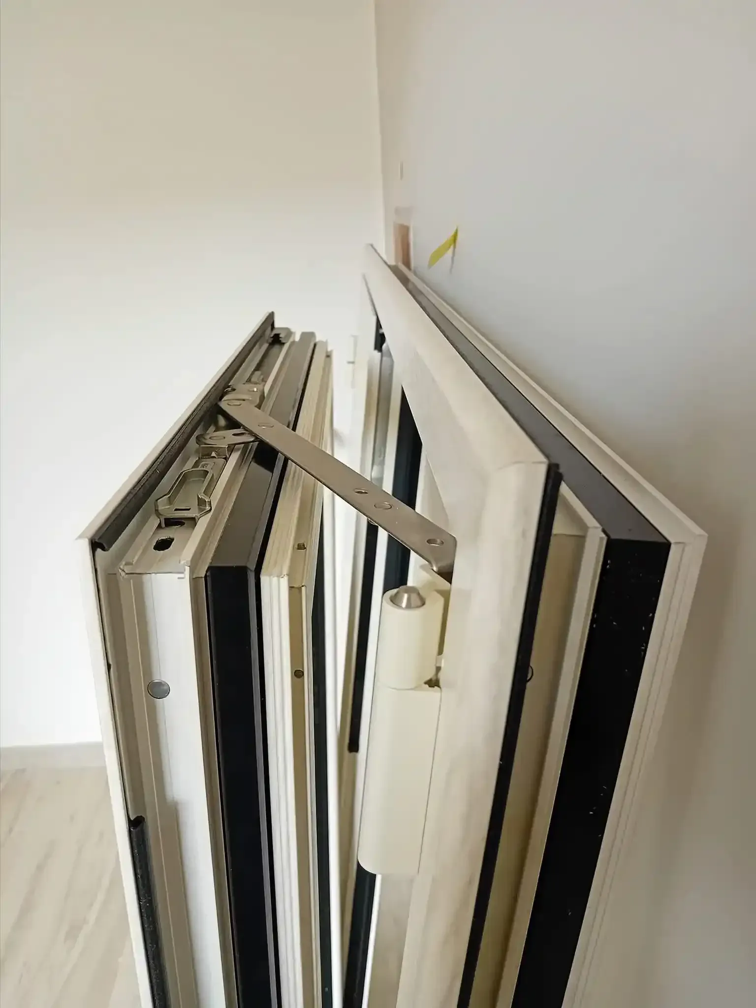 Telaio per porta pieghevole, bianco e nero, con braccio meccanico e meccanismo di chiusura a molla, montato a parete.