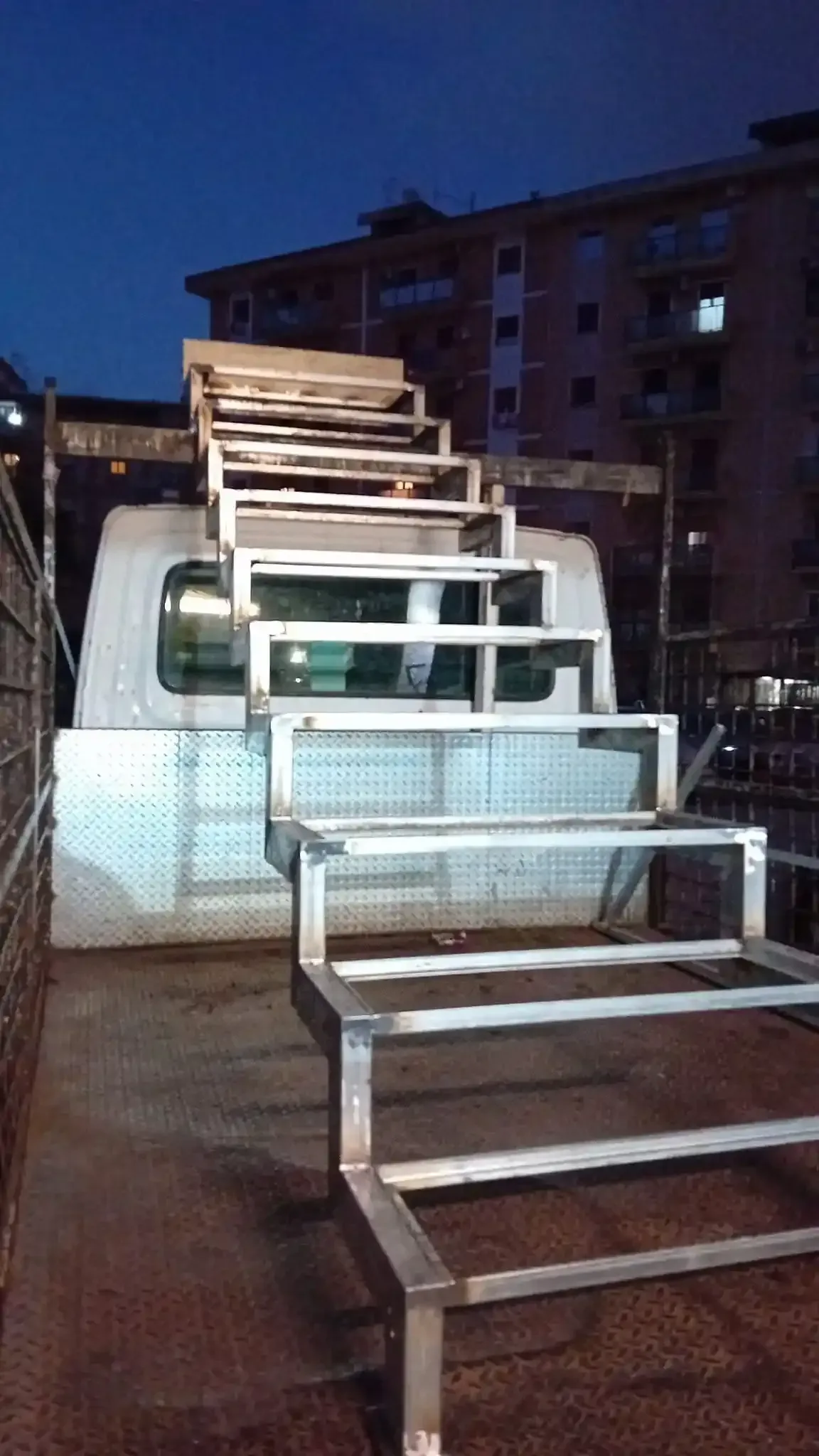 Scala metallica fissata al retro di un camion bianco. I gradini salgono e scendono. Ambientazione serale.