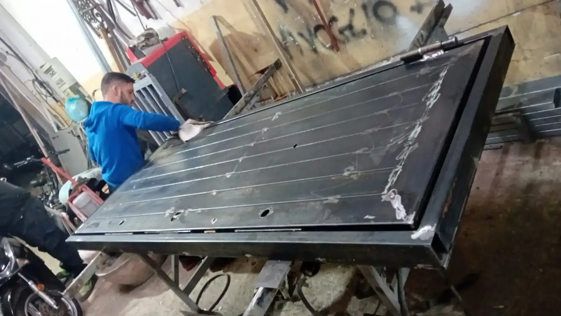 Uomo che pulisce una grande porta di metallo su un banco da lavoro in un'officina.