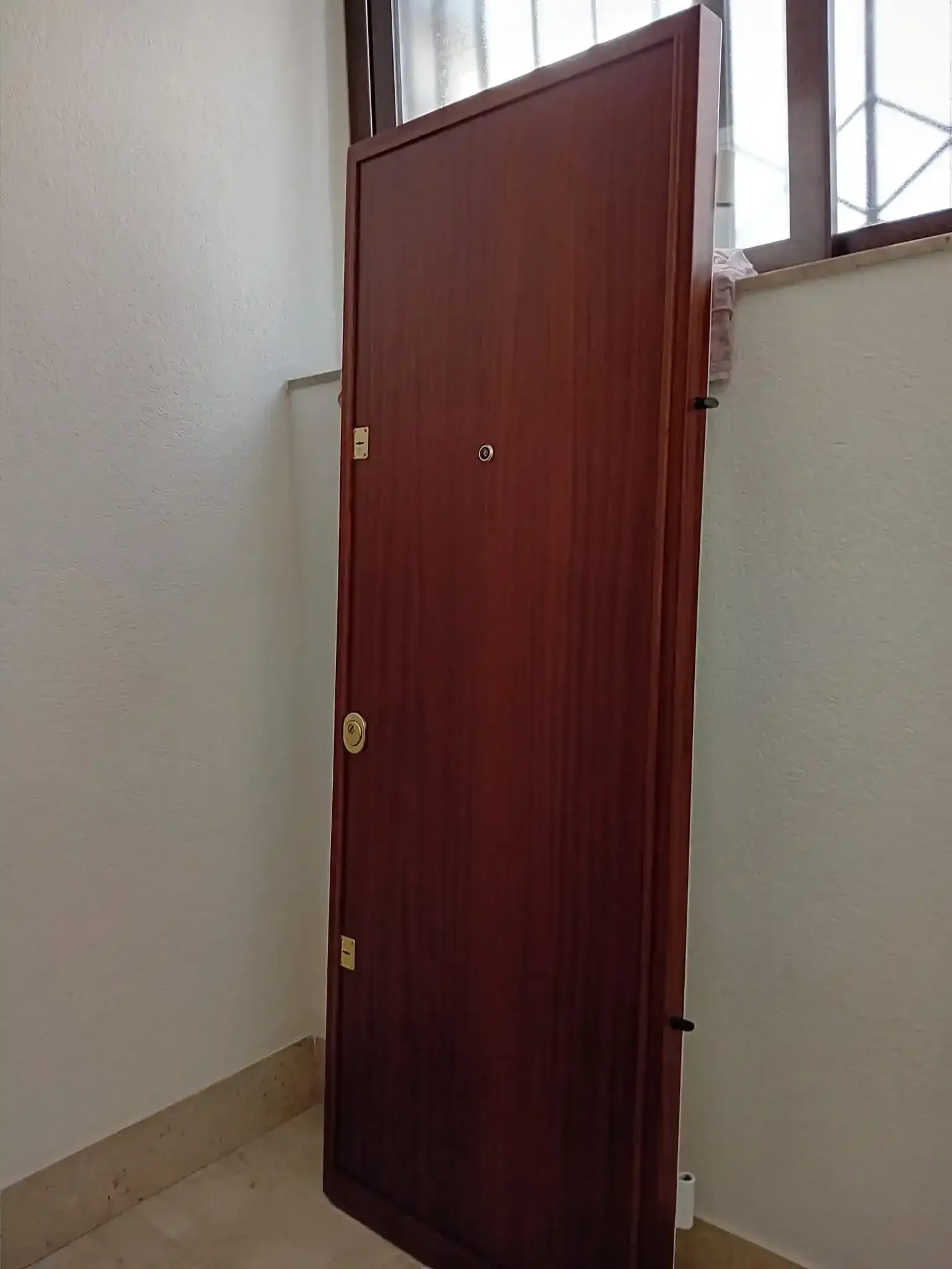 Una porta di legno marrone chiusa in un angolo contro le pareti bianche, con una piccola finestra visibile.