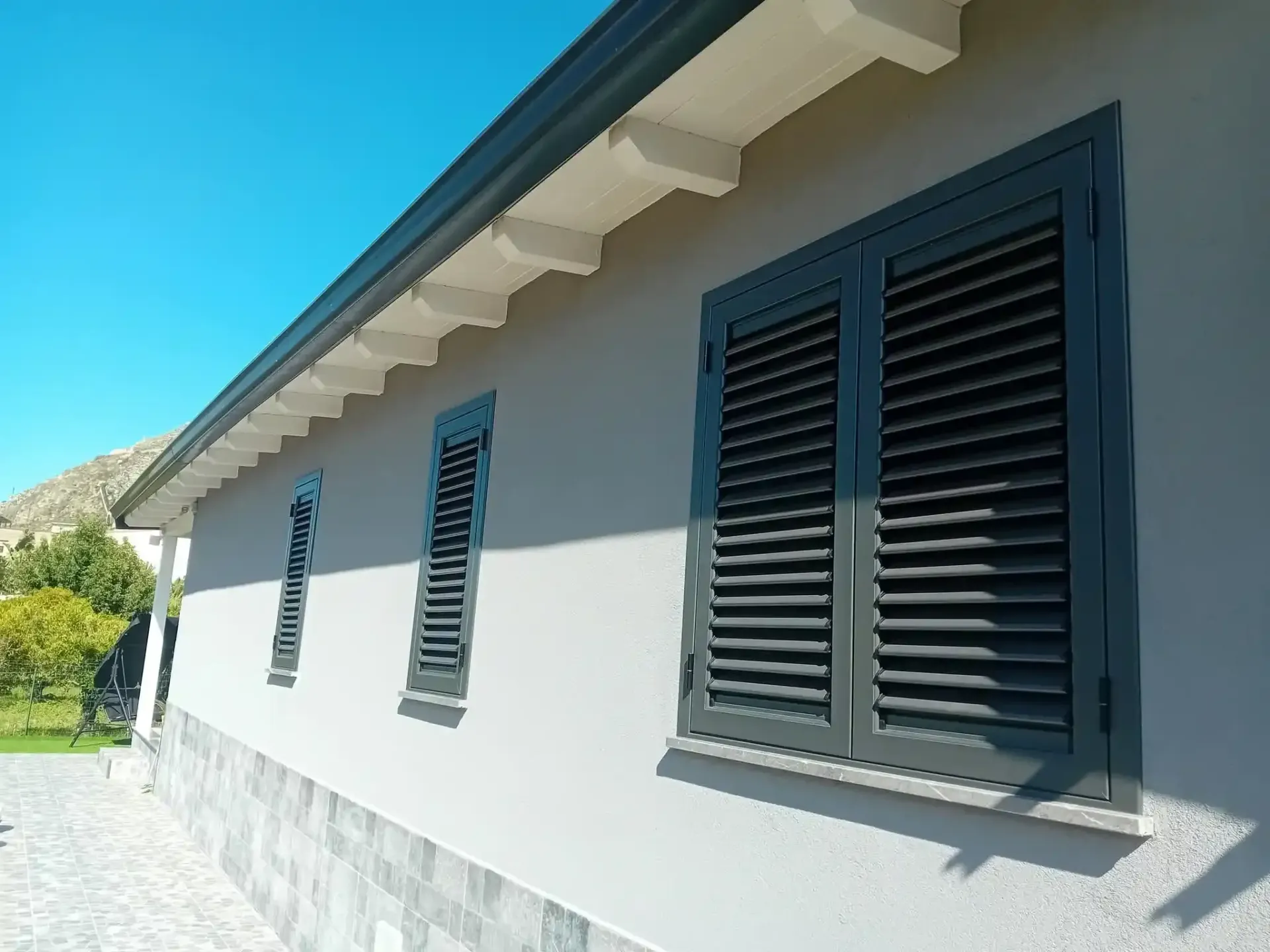 Casa grigia con persiane verdi, finiture bianche e cielo azzurro.