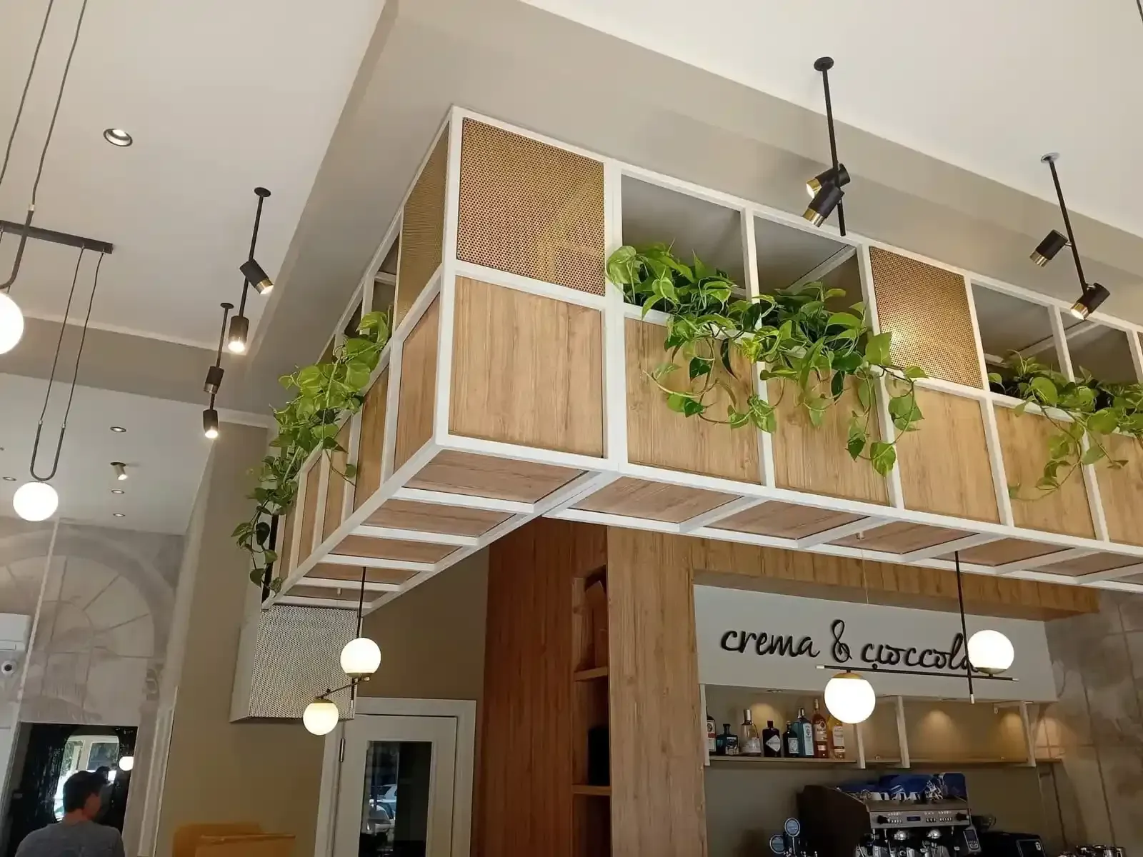 Interno di un ristorante con fioriere sospese che ospitano piante verdi, illuminazione decorativa e un bancone.