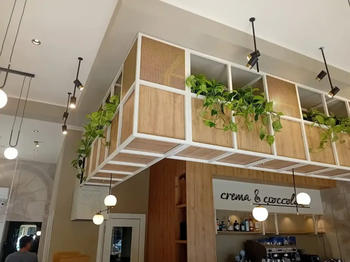 Interno di un ristorante con fioriere sospese che ospitano piante verdi, illuminazione decorativa e un bancone.