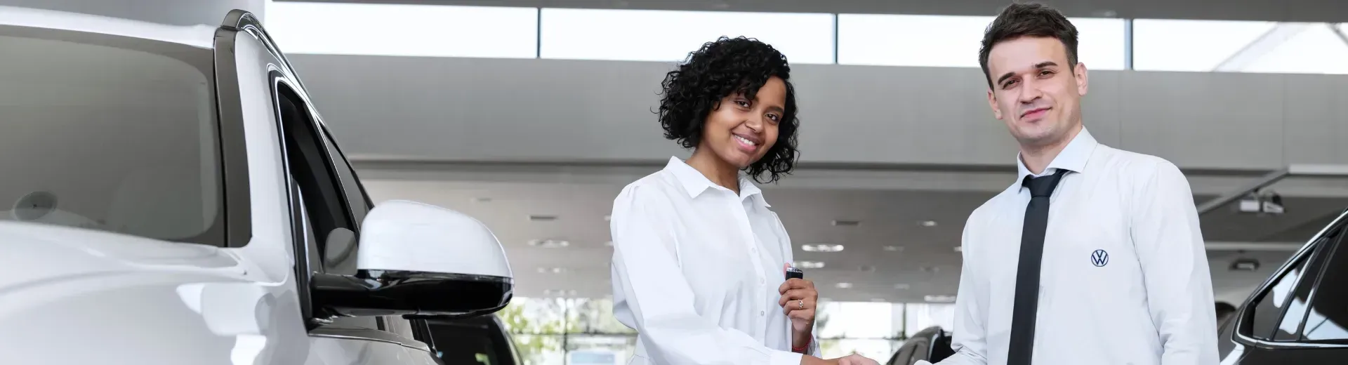 Mulher e homem apertando as mãos em uma concessionária de automóveis, ambos sorrindo. 