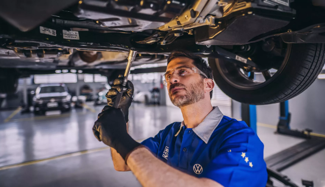 Mecânico de uniforme azul trabalhando na parte inferior de um carro em uma garagem.