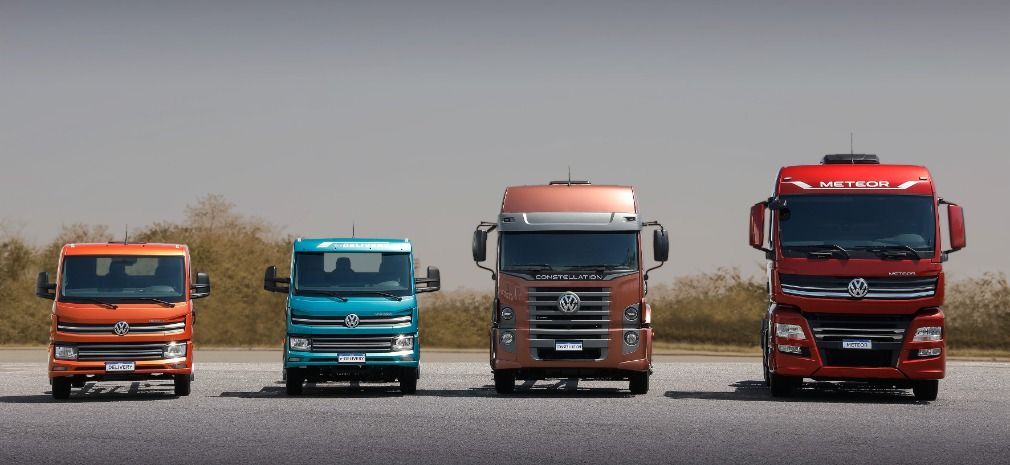 Four different-sized Volkswagen trucks lined up on a gray surface, with an overcast sky in the background.