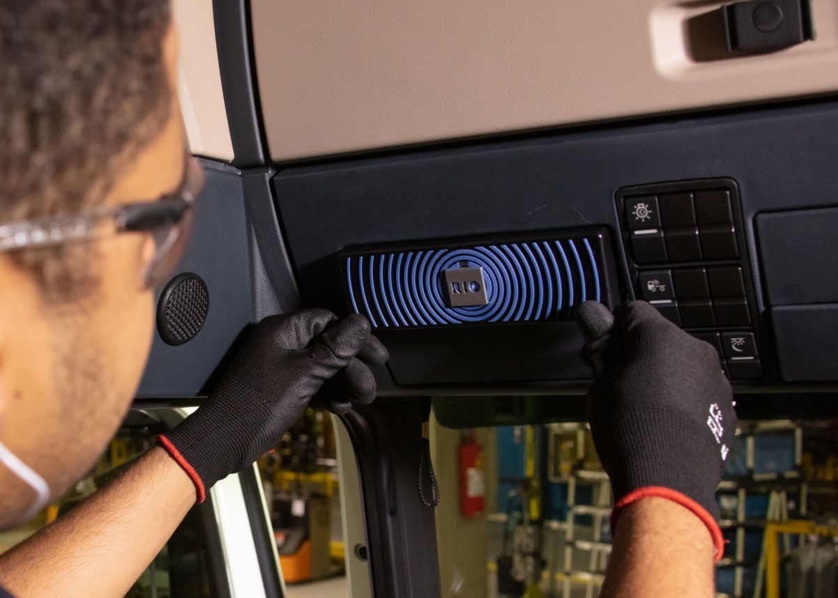 Uma pessoa usando óculos de segurança e luvas instalando um painel de controle preto com ondas azuis radiantes em um veículo.