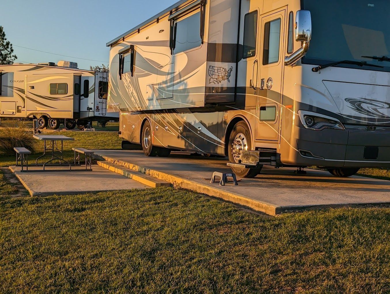 A large RV parked in a campground with a concrete pad, grass, and other RVs in the background.
