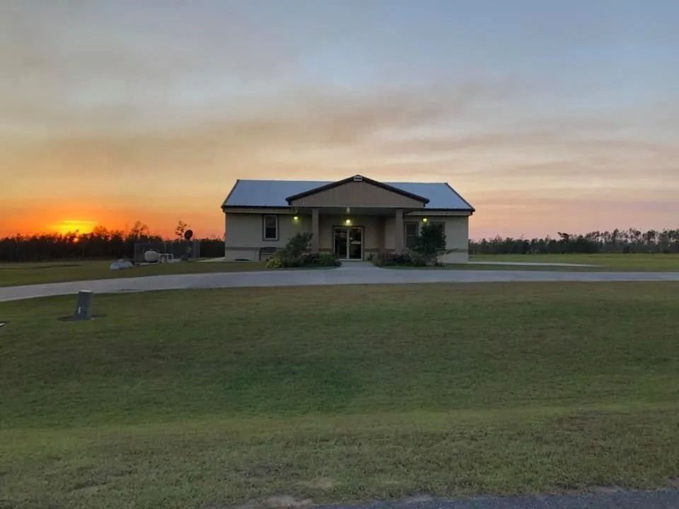 A single-story beige building with a dark roof, on a grassy lawn at sunset.