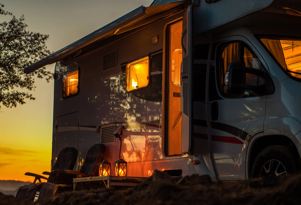 RV parked at dusk with lights on, awning extended, surrounded by lanterns and trees.