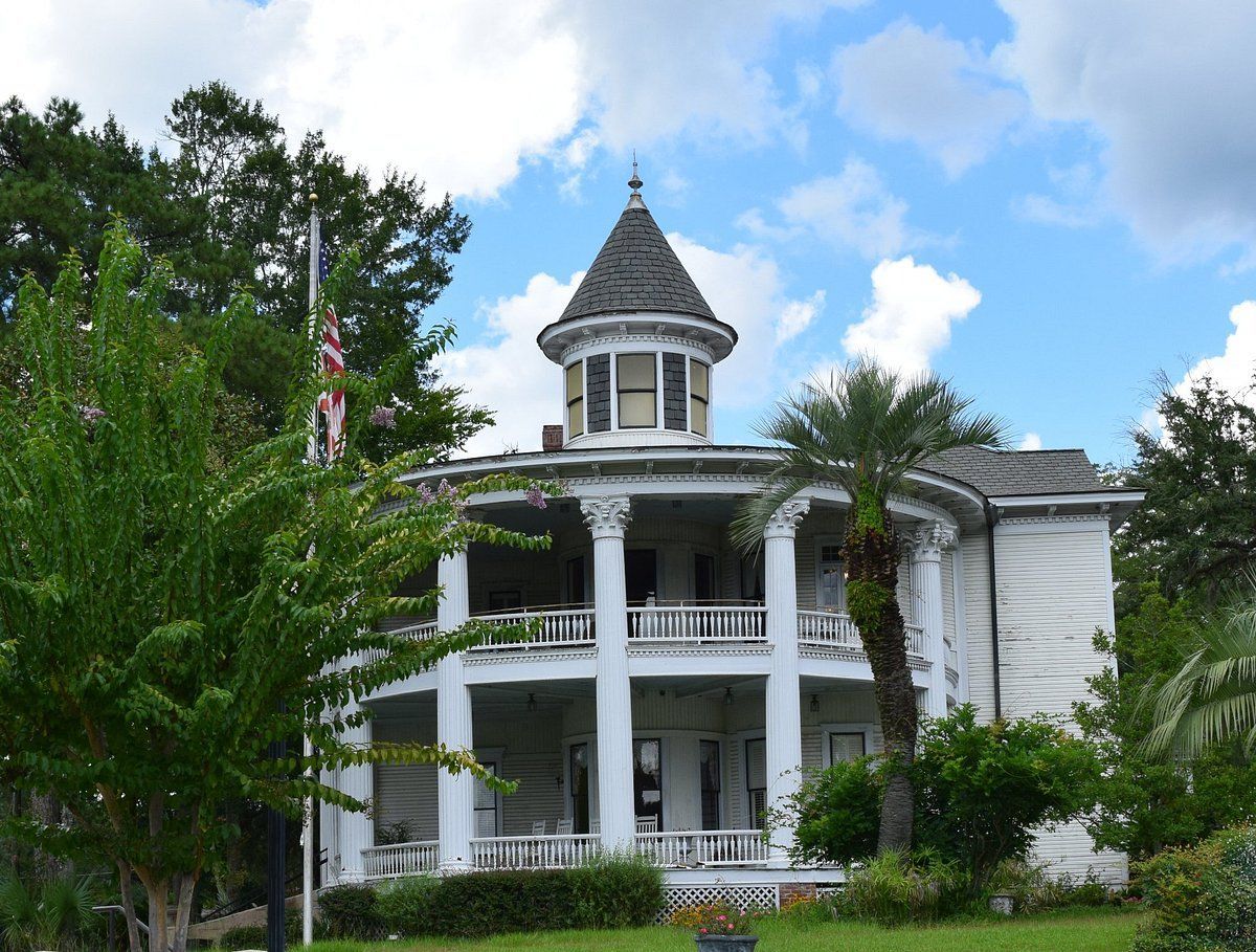 Two-story white house with porch and turret under a blue sky with clouds; an American flag is visible.