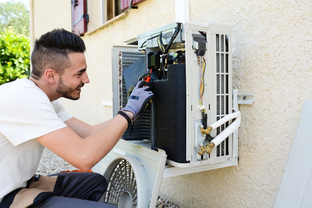 A Man Is Fixing An Air Conditioner On The Side Of A Building — Cairns Excel Electrics In Bungalow, QLD