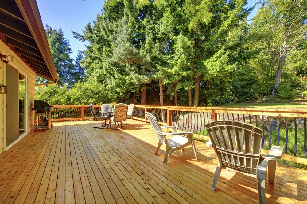 Wooden deck with chairs, table, and grill, overlooking a green yard and tall trees.