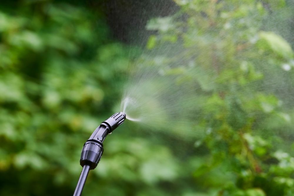 Sprayer nozzle emitting water mist into green foliage.