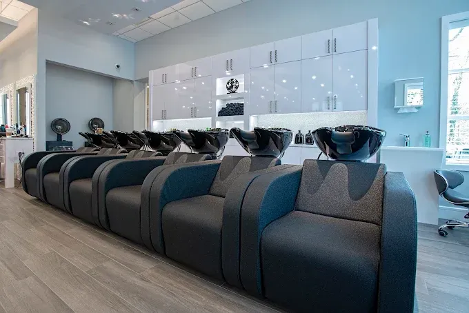 Hair salon with wash stations and dark gray chairs. Light walls and cabinets.