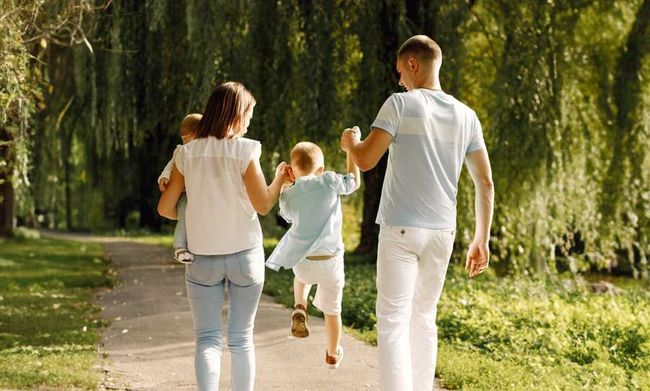 Eine Familie geht Händchen haltend einen Weg im Park entlang.