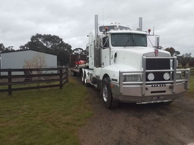 a white semi truck is parked in a grassy field next to a fence .