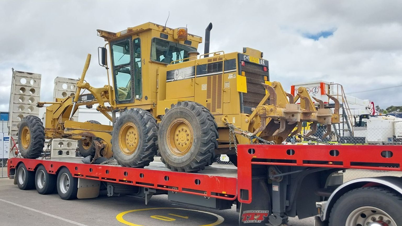 a white semi truck is carrying a forklift on a trailer .