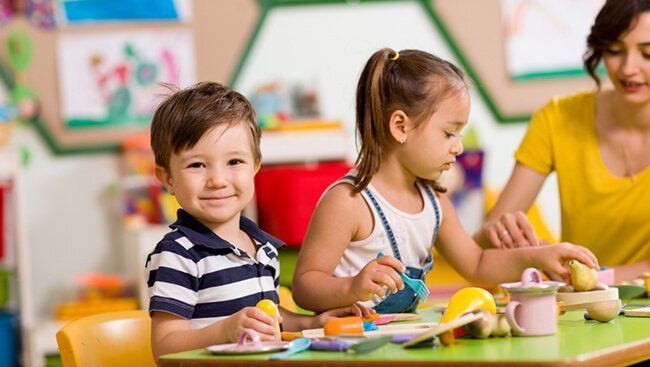 A group of montessori children are sitting at a table in a classroom working with materials.