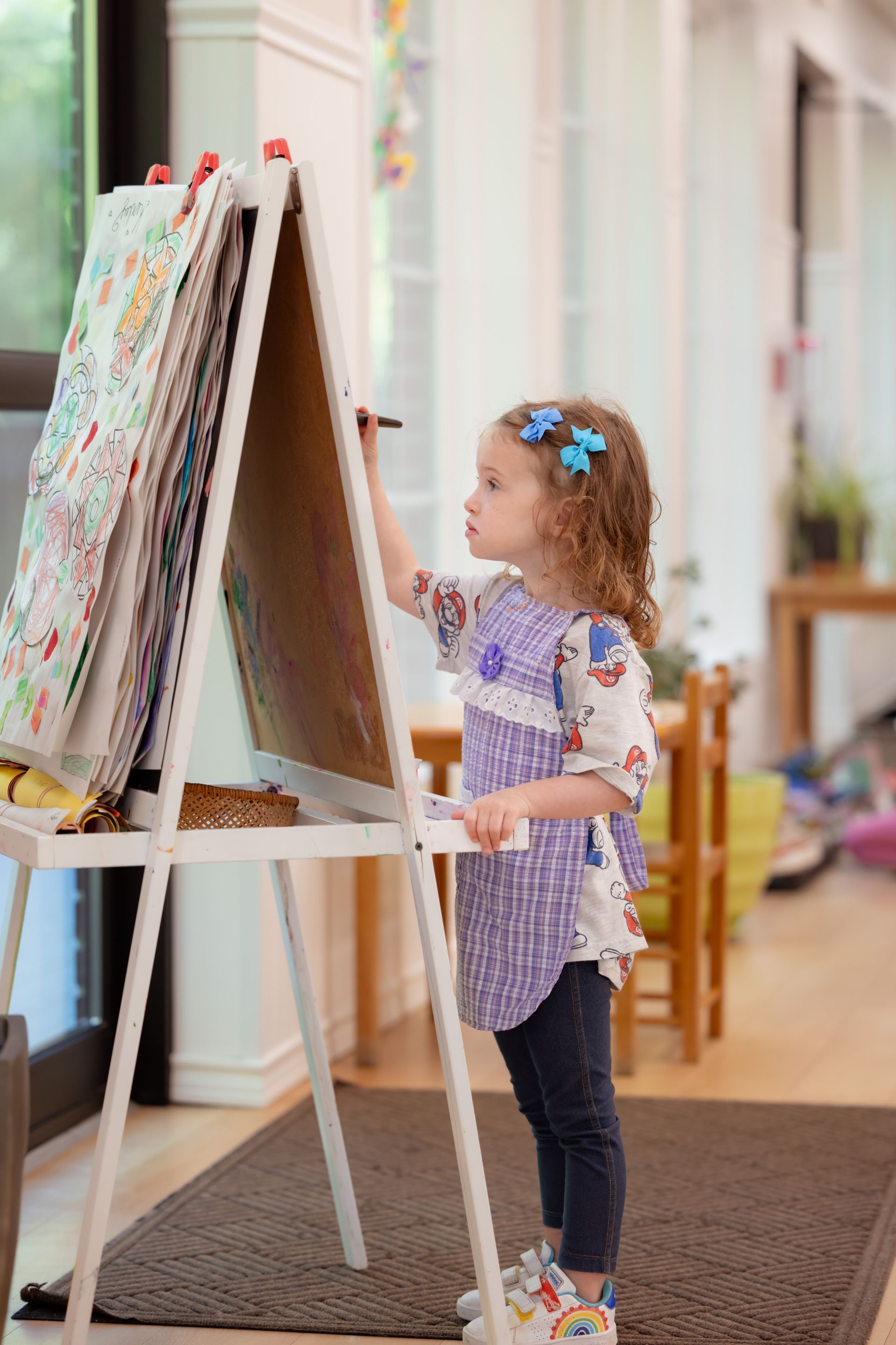 A little girl is painting on an easel in a room.