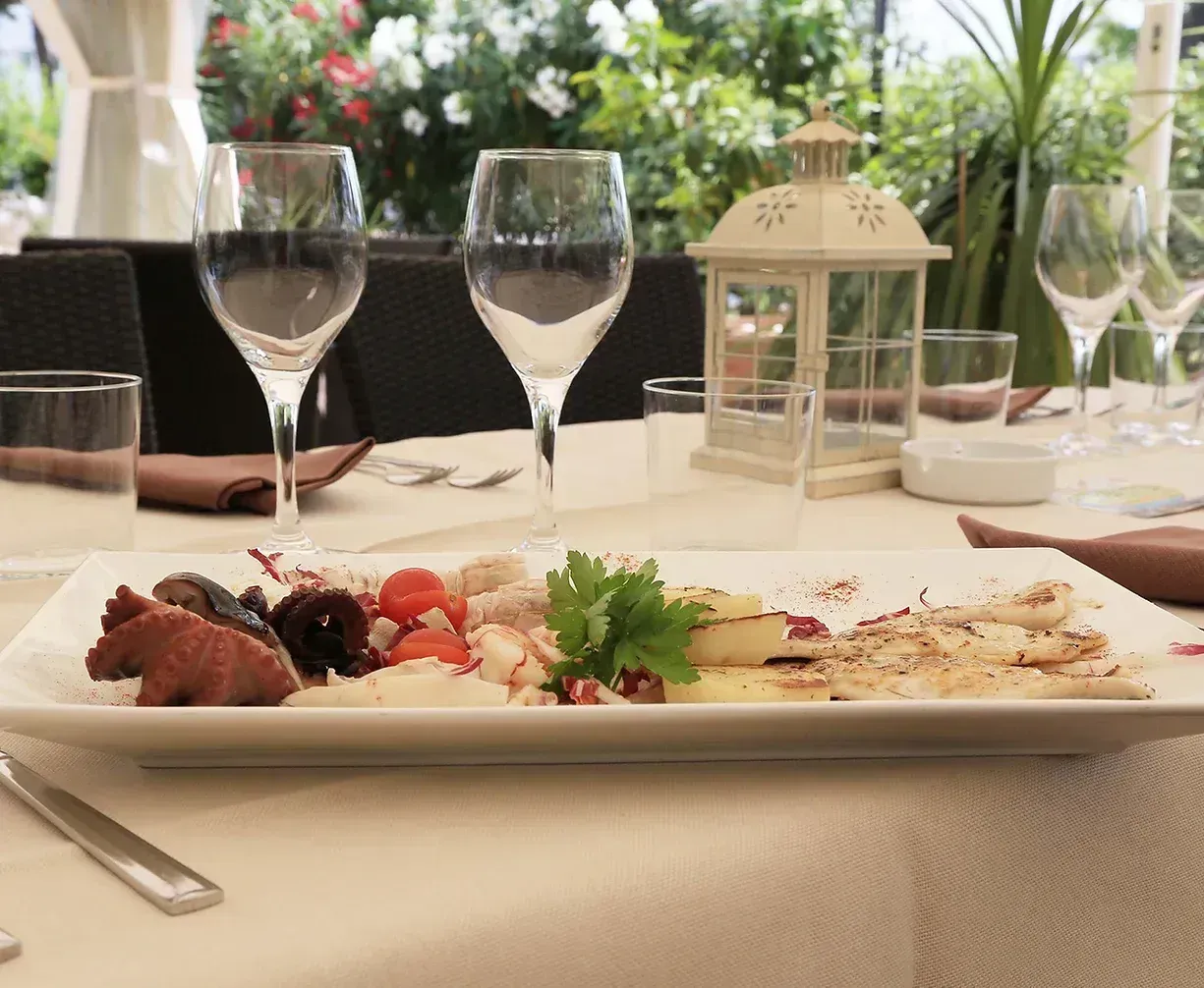 Un piatto di cibo con bicchieri di vino su un tavolo apparecchiato per cenare all'aperto.
