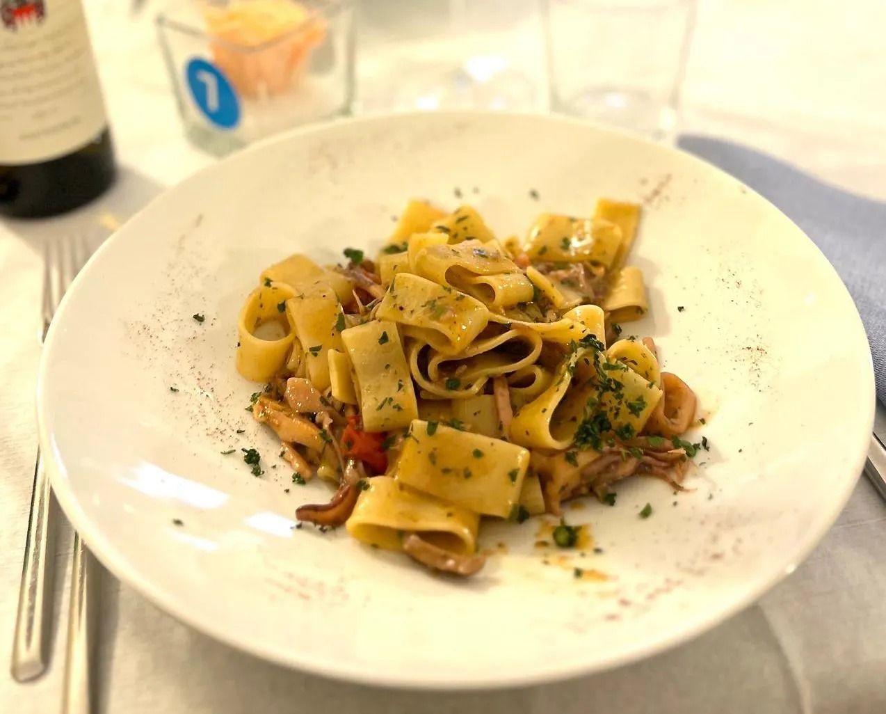 Piatto di pasta con tagliatelle larghe, frutti di mare ed erbe aromatiche su un piatto bianco.