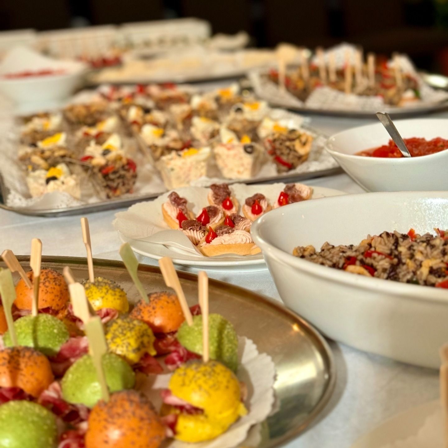 Tavolo da buffet con vari antipasti, tra cui spiedini, quadrotti e ciotole di cibo, all'interno.