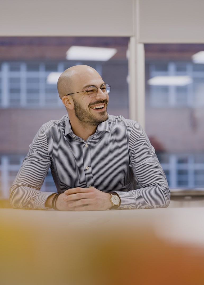 A man is sitting at a table in front of a window and smiling.