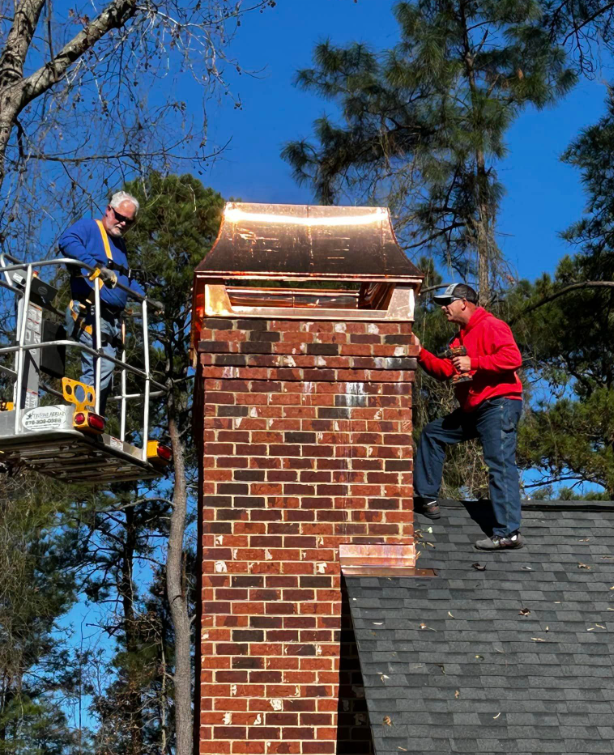 Two Men Are Working On A Brick Chimney On A Roof — Richmond Hill, GA — A Plus